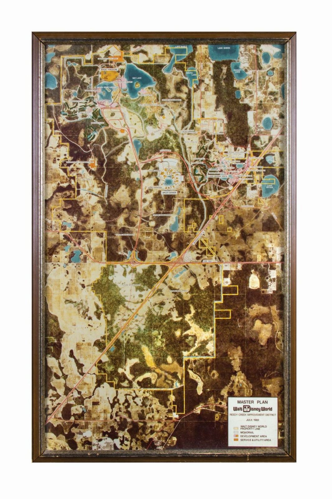 A framed wall-mounted master plan: a colour aerial photomosaic of the Walt Disney World property with the property line, monorail, development areas and service and utility areas overlaid, and a printed legend card at lower right.